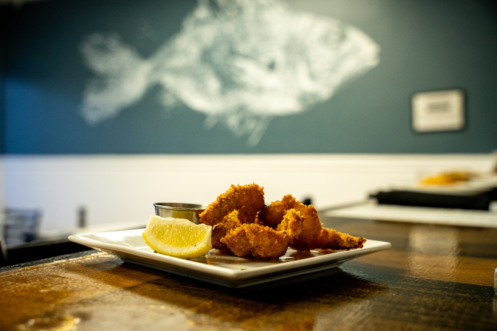 Crispy coconut shrimp with lemon, fish mural in background — Luc's Seafood & Grill