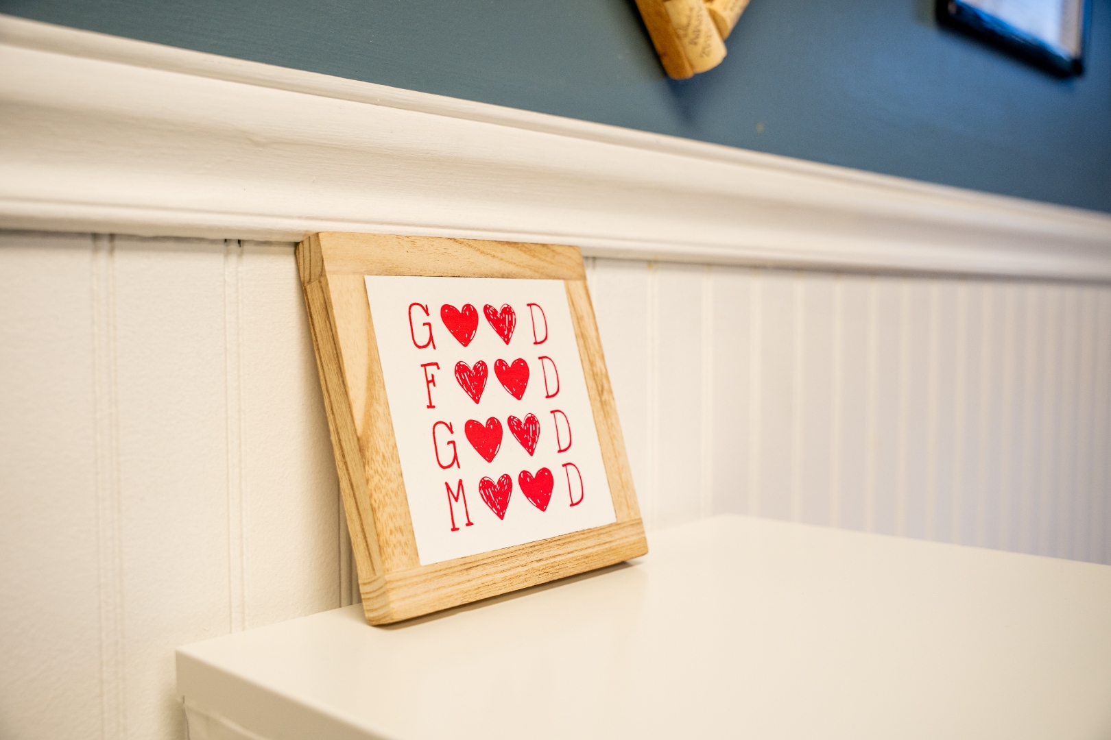 Framed &lsquo;Good Food Good Mood&rsquo; art piece on the dining room shelf at Luc's